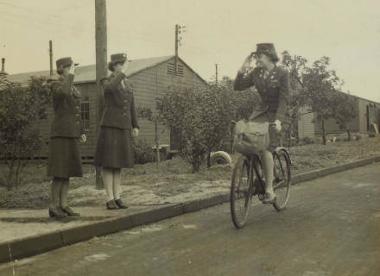 1st Lt Hilda T Berry riding her bicycle and saluting fellow WACs. (Digital archive reference MC 371/814)