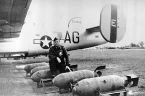 A serviceman sitting in a row of bombs at Hardwick Airfield.